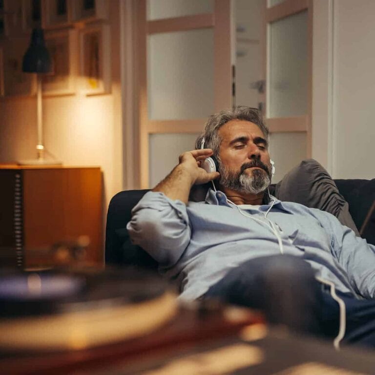Relaxed man listening to music while reading a magazine at home, representing investment and financial management.