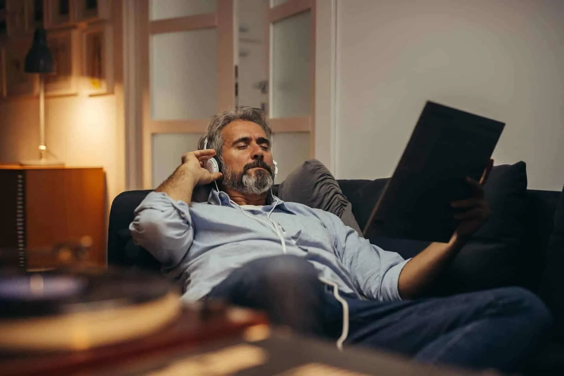 Relaxed man listening to music while reading a magazine at home, representing investment and financial management.