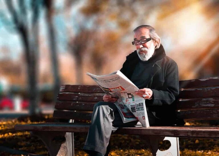 Elderly man reading newspaper on park bench in autumn setting, financial news.